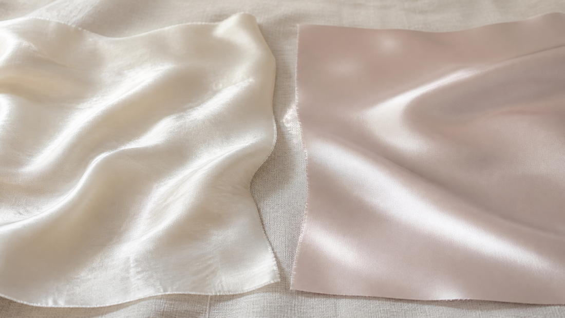 Ivory silk swatch and flatter synthetic satin swatch side by side on cream linen under raking light