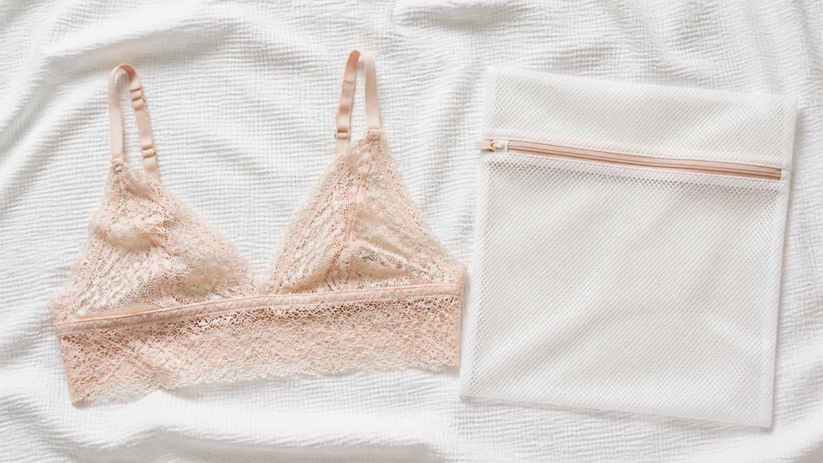 Delicate blush lace bralette laid flat next to a mesh laundry wash bag on white towel