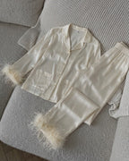 Darette Feather Weight Silk Set in Ivory - satin pajama set with feather cuffs, laid flat on a knit throw