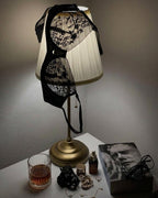 Darette Good Habit Lace Set in Noir styled on a lamp beside a nightstand with drinks and books