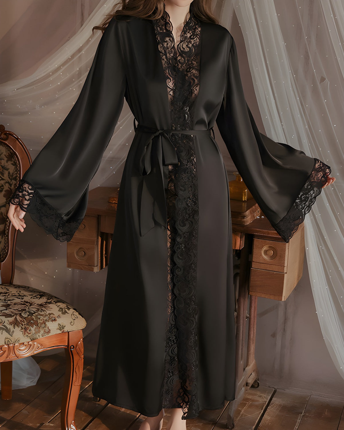 Darette Late Start Robe in Noir - long satin robe with lace cuffs, standing beside a chair