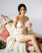 Darette Nightcap Set in Champagne - front view seated in the lace-trim satin slip and robe, holding a feather