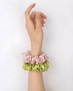 Darette silk scrunchies worn stacked on the wrist in pink and green, showing the ruffled satin texture