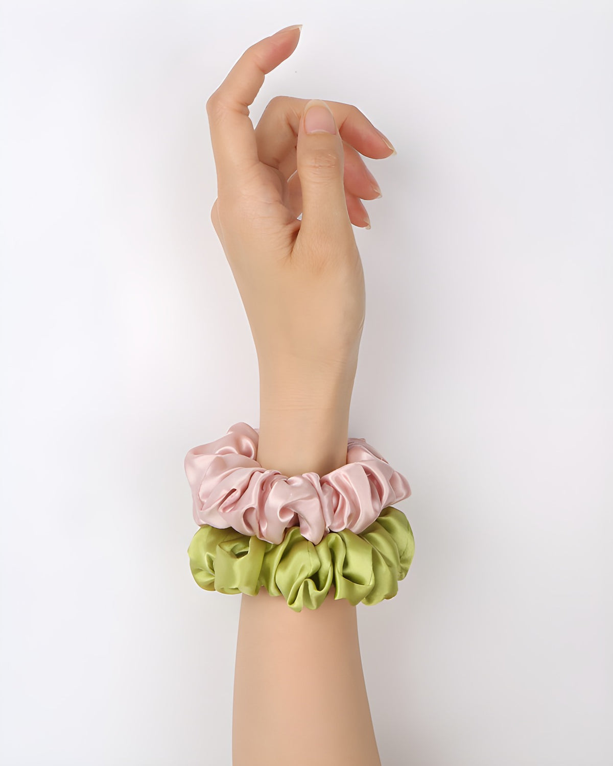 Darette silk scrunchies worn stacked on the wrist in pink and green, showing the ruffled satin texture